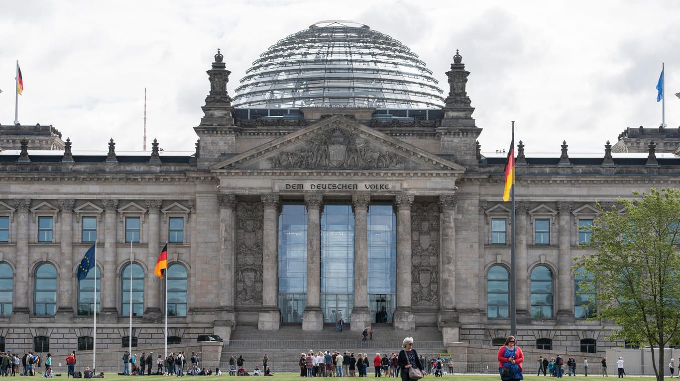 Touristen gehen in Berlin über die Wiese vor dem Reichstag.
