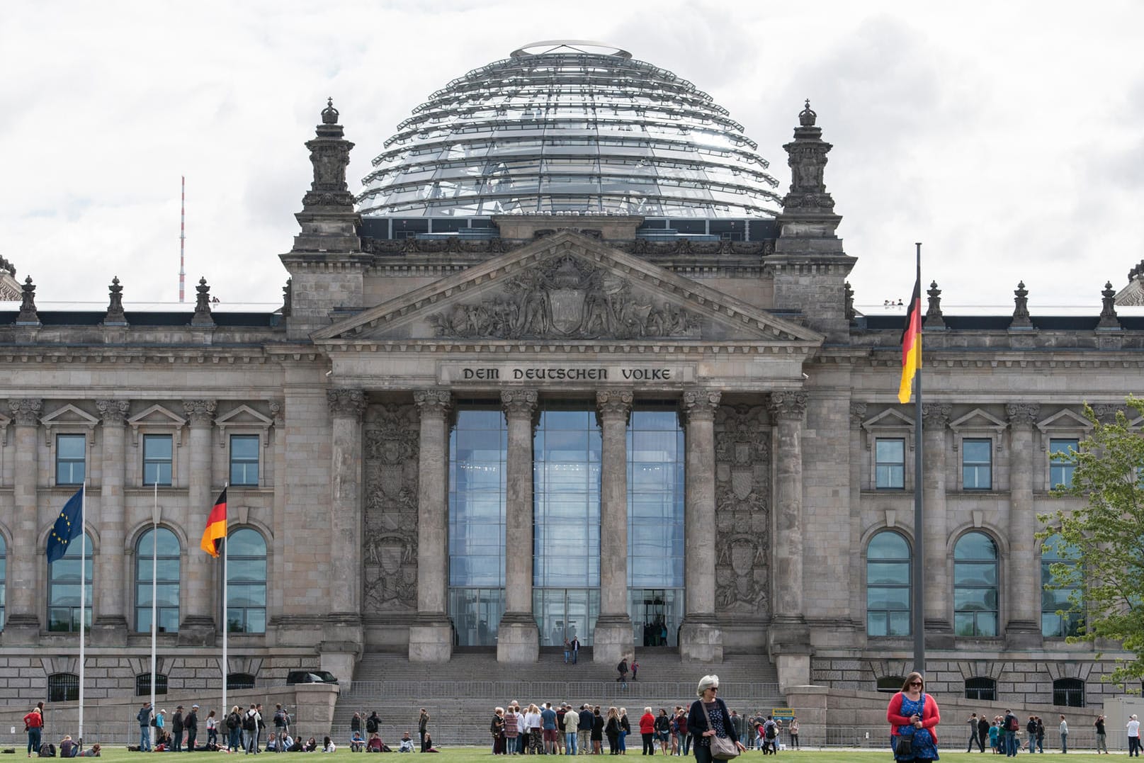 Touristen gehen in Berlin über die Wiese vor dem Reichstag.