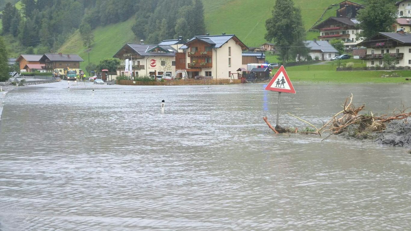 Ein Straßenschild schaut in Großarl nach Murenabgängen auf einer überschwemmten Straße über dem Wasser heraus.
