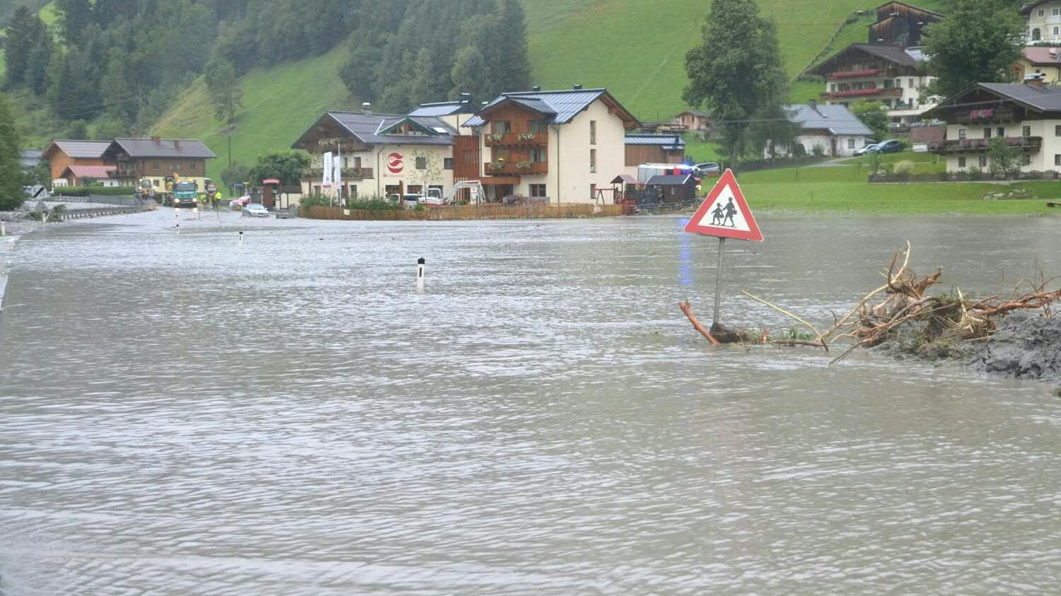Ein Straßenschild schaut in Großarl nach Murenabgängen auf einer überschwemmten Straße über dem Wasser heraus. Ein Straßenschild schaut in Großarl nach Murenabgängen auf einer überschwemmten Straße über dem Wasser heraus.