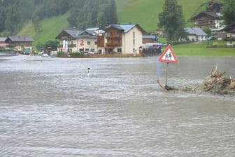 Ein Straßenschild schaut in Großarl nach Murenabgängen auf einer überschwemmten Straße über dem Wasser heraus.