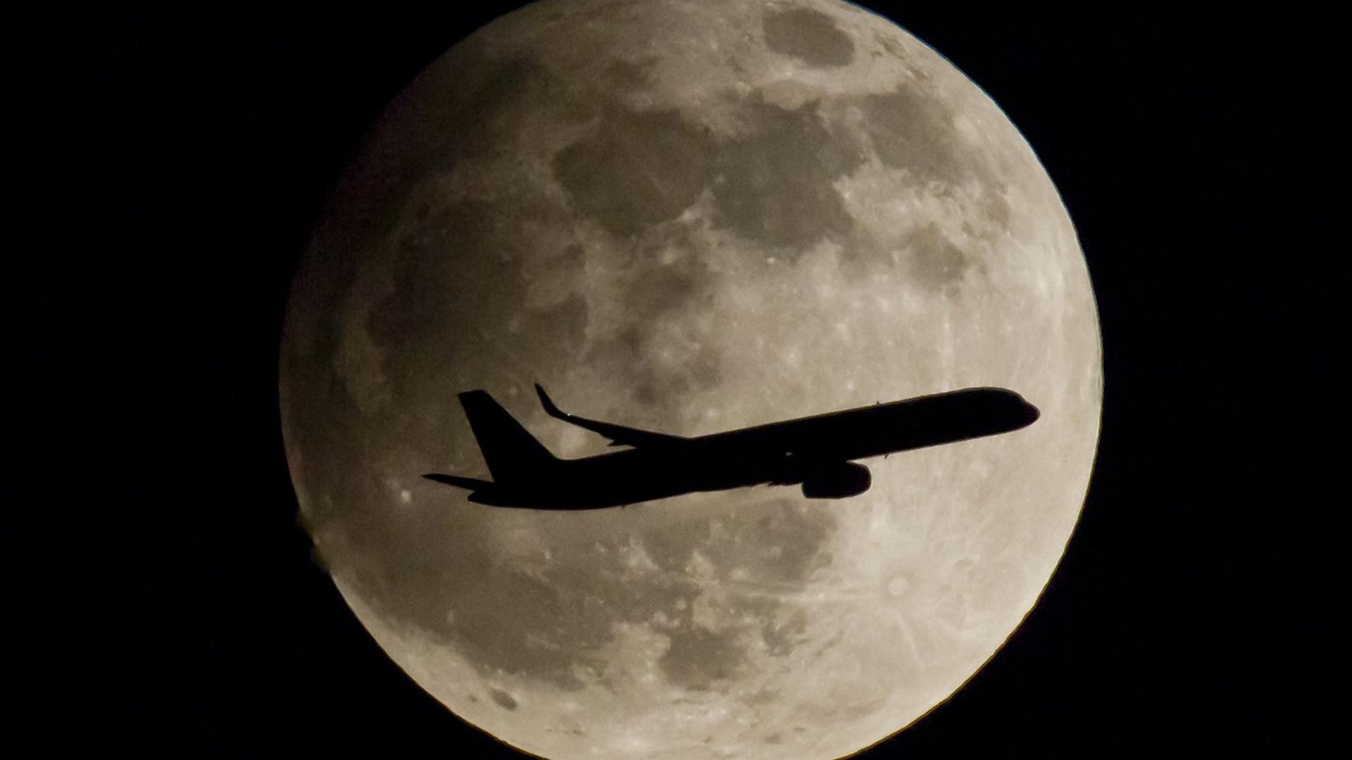 Ein Passagierflugzeug passiert den Vollmond, der am wolkenlosen Nachthimmel steht. Das Bild entstand bei der partiellen Mondfinsternis 2013.