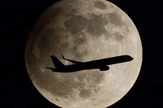 Ein Passagierflugzeug passiert den Vollmond, der am wolkenlosen Nachthimmel steht. Das Bild entstand bei der partiellen Mondfinsternis 2013.