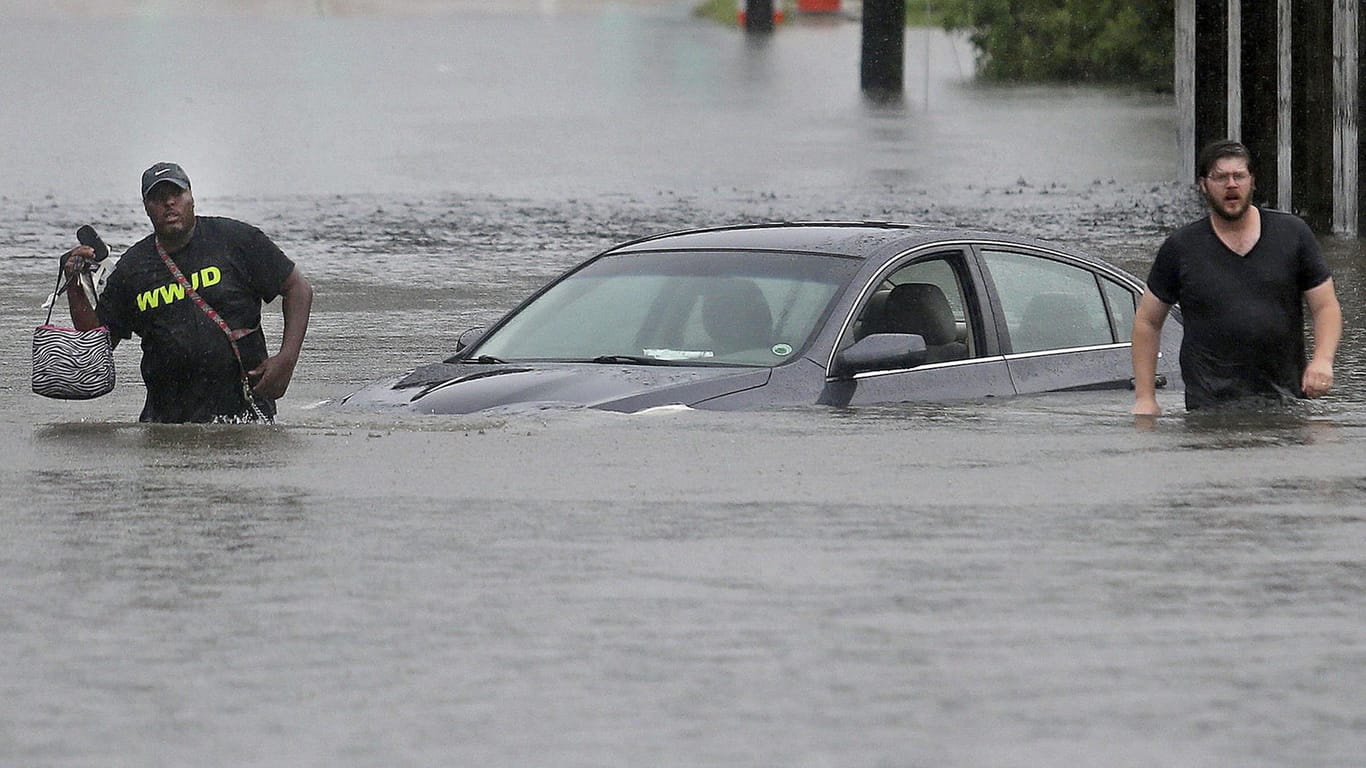 Zwei Männer waten in New Orleans über eine überflutete Straße an einem Auto vorüber.