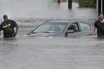 Zwei Männer waten in New Orleans über eine überflutete Straße an einem Auto vorüber.