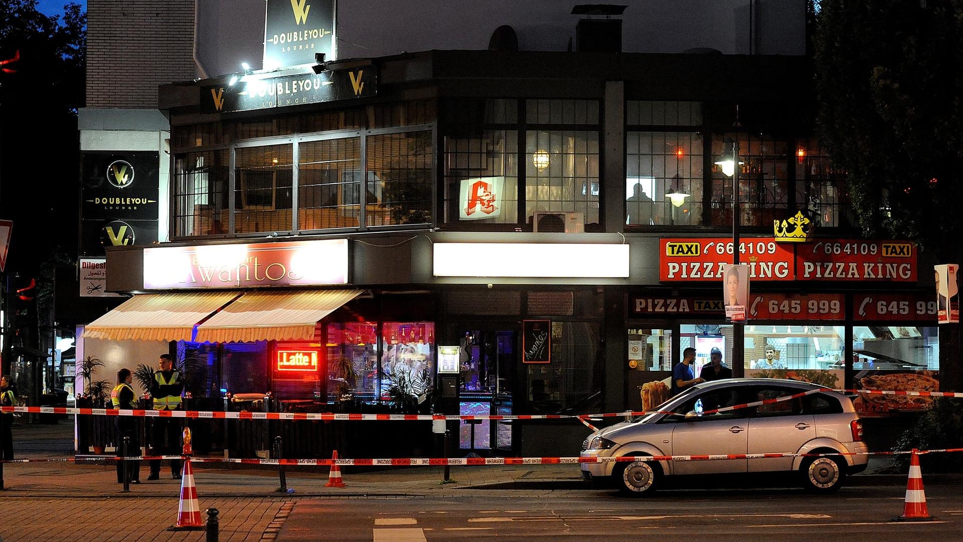 Polizisten stehen in einem mit Flatterband abgesperrten Bereich vor einem Bistro in Wuppertal, wo ein Mann lebensgefährlich verletzt worden ist.