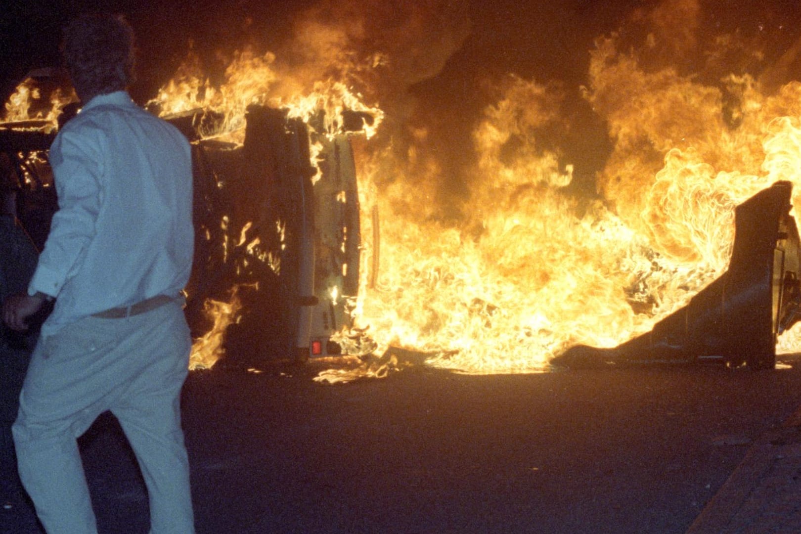 Ein Mann steht am 27.08.1992 vor einem brennenden Pkw auf einer Straße am zentralen Asylbewerberheim von Mecklenburg-Vorpommern in Rostock-Lichtenhagen.