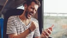 Mann hört freudig Musik im Zug per Handy
