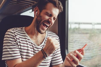 Mann hört freudig Musik im Zug per Handy