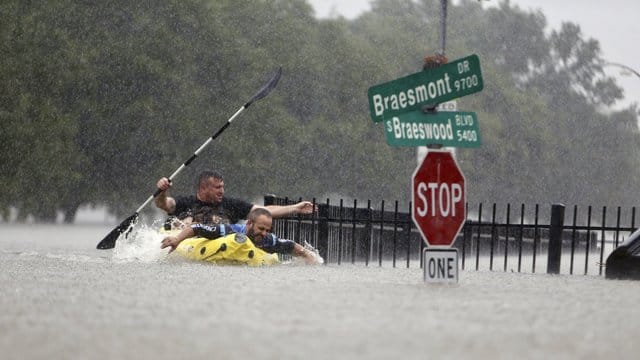 In Houston rudern zwei Männer bei heftigem Regen auf einer überfluteten Straße. In Houston rudern zwei Männer bei heftigem Regen auf einer überfluteten Straße.