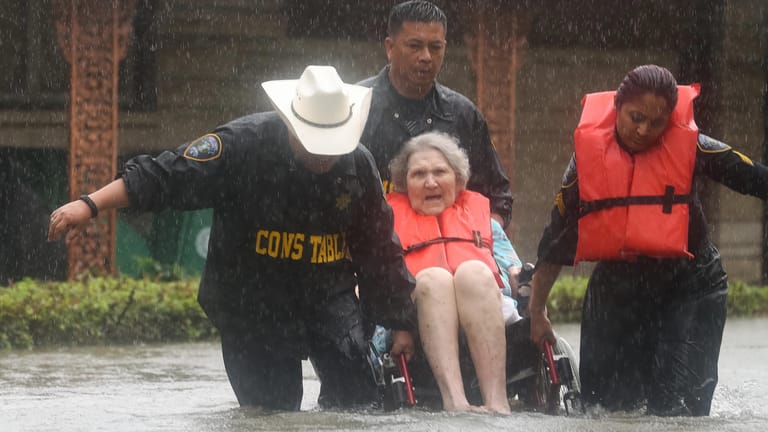 Polizisten tragen in Houston eine Frau im Rollstuhl aus ihrem überfluteten Haus.