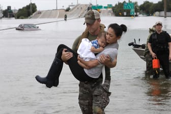 Ein Polizist bringt eine Frau und ihren Sohn von einer überfluteten Straße in Houston in Sicherheit.