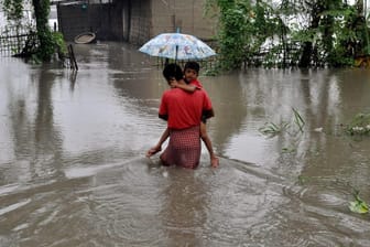 Ein Vater trägt in Lakhimpur (Indien) seinen Sohn und watet durch ein überflutetes Gebiet.