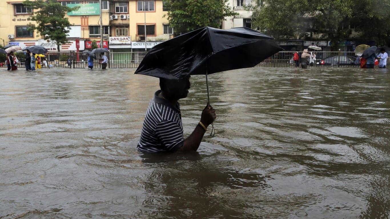 Ein Mann watet in Mumbai (Indien) über eine überflutete Straße.