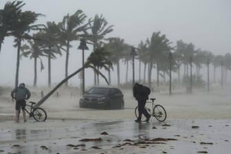 Zwei Männer schieben in Fort Lauderdale, Florida, ihre Fahrräder entlang einer überfluteten Straße.