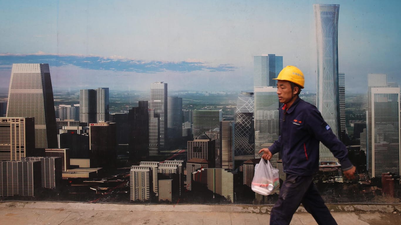 Ein Bauarbeiter läuft in Peking an einem Poster vorbei, das für zukünftige Bauvorhaben wirbt.