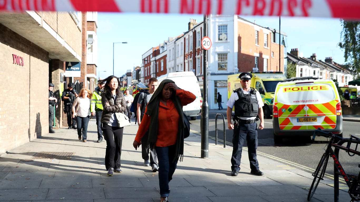 People walk past an armed police officer near Parsons Green tube station in London