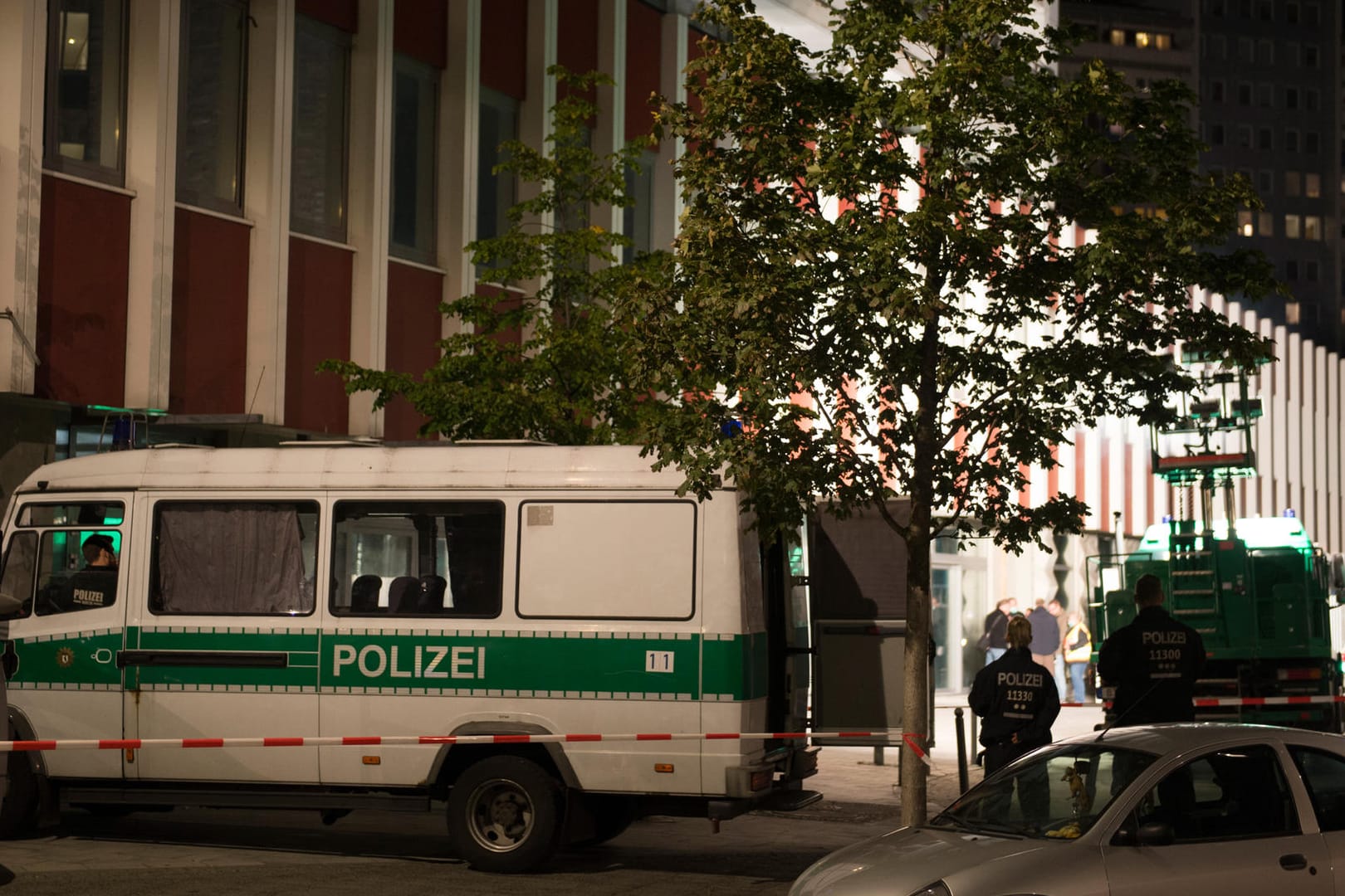 Einsatzfahrzeuge der Polizei stehen in Berlin-Mitte am Abend vor einer Absperrung. Dort wurde auf einem Platz nahe einem Hochhaus eine Leiche gefunden. Ein Zelt wurde über den Fundort gestellt, bevor die Kriminaltechniker ihre Arbeit aufnahmen.