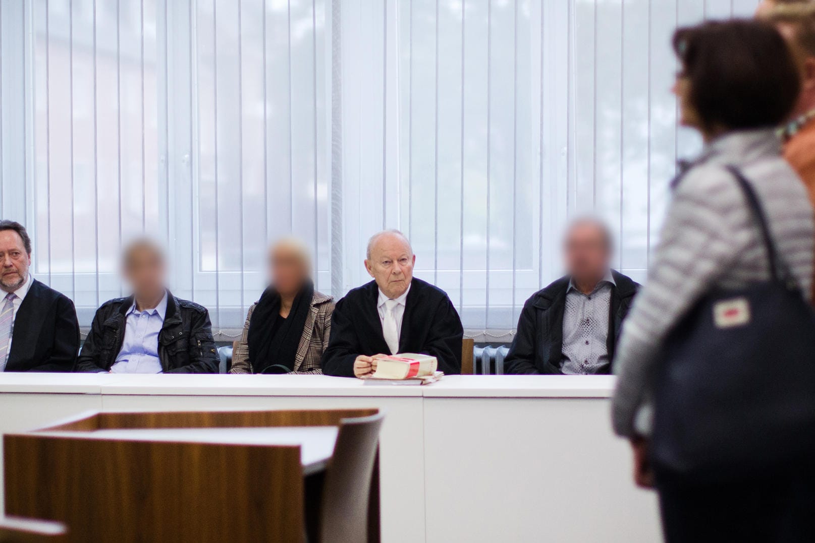Die drei Angeklagten warten in Essen im Gerichtssaal neben ihren Anwälten auf den Prozessbeginn. Die Angehörigen des Opfers stehen rechts.
