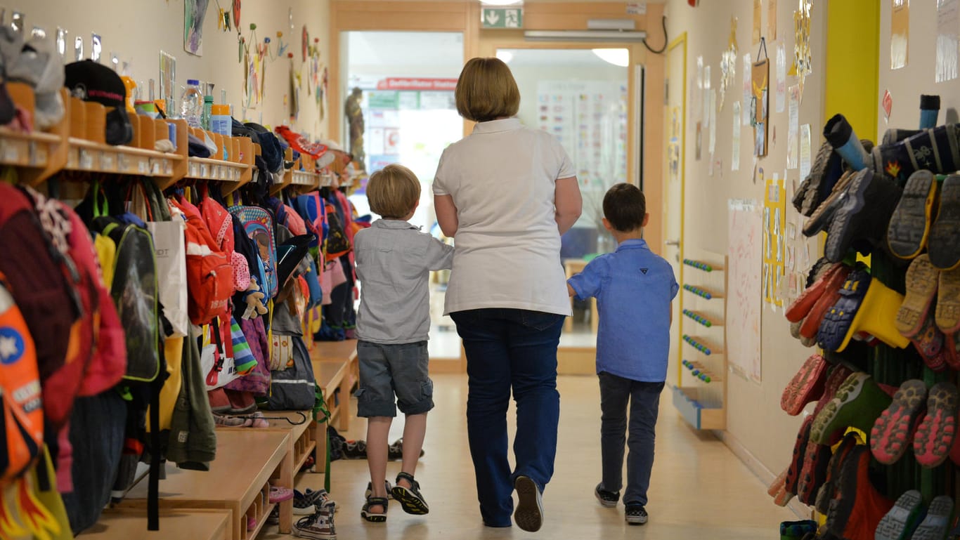 Eine Erzieherin geht in einem Kindergarten mit zwei Kindern über den Flur.