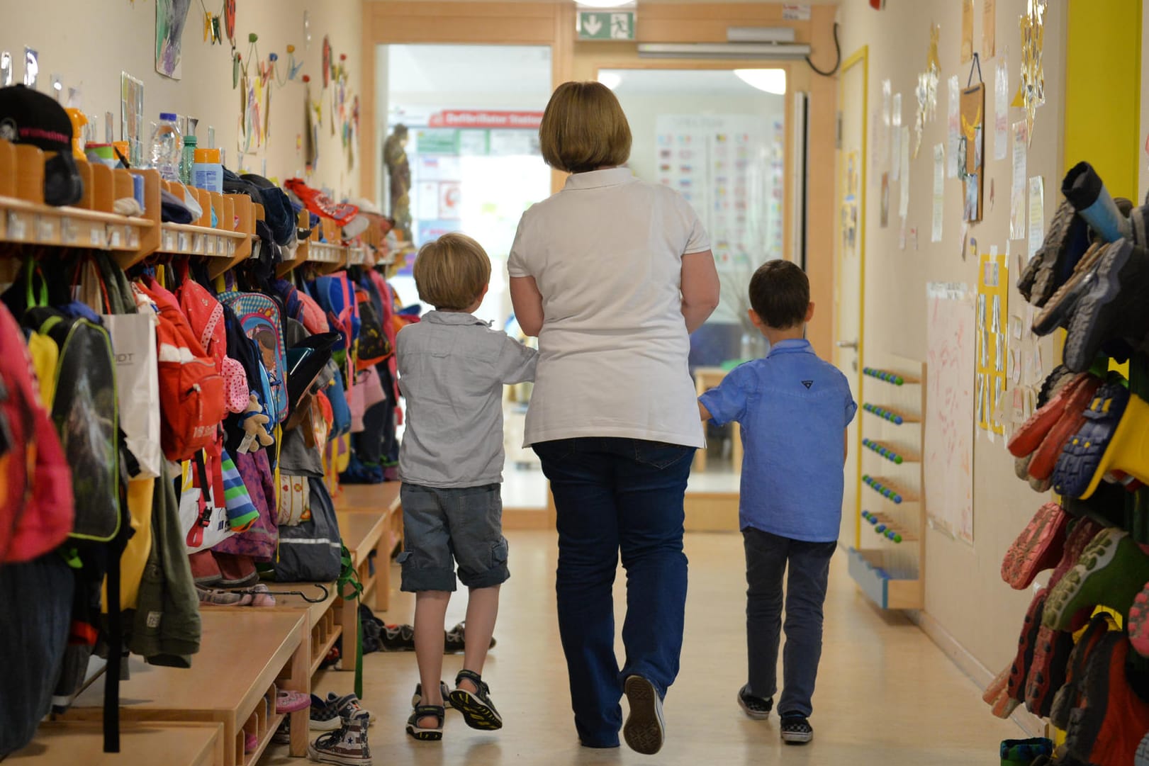 Eine Erzieherin geht in einem Kindergarten mit zwei Kindern über den Flur.