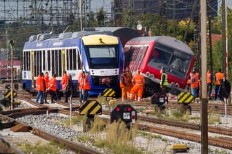 Diverse Mitarbeiter der Bahn stehen in Augsburg neben einem verunglücktem Personenzug.