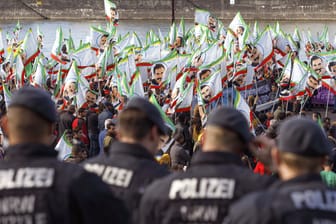 Beim Kurdischen Kulturfestivalt in Köln stehen Teilnehmer mit Fahnen, auf denen Porträts des PKK-Führers Öcalan zu sehen sind. Davor stehen Polizisten und beobachten die Situation.