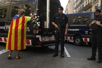 Ein Frau mit einer "Estelada"-Flagge steckt Nelken an einen Polizeiwagen.