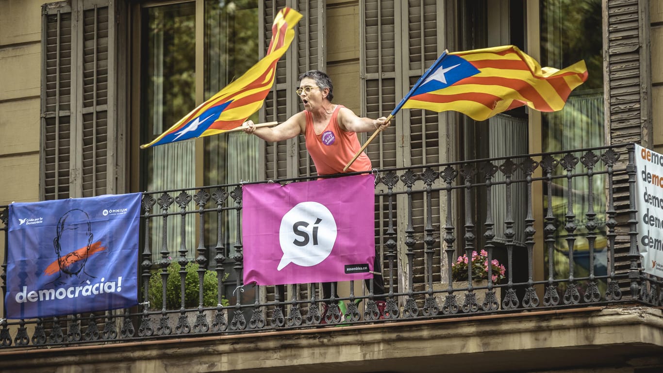 Eine Frau schwenkt in Barcelona (Spanien) auf einem Balkon zwei Fahnen Kataloniens, während Studenten für das Referendum über eine Unabhängigkeit Kataloniens demonstrieren.