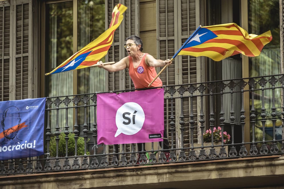 Eine Frau schwenkt in Barcelona (Spanien) auf einem Balkon zwei Fahnen Kataloniens, während Studenten für das Referendum über eine Unabhängigkeit Kataloniens demonstrieren.