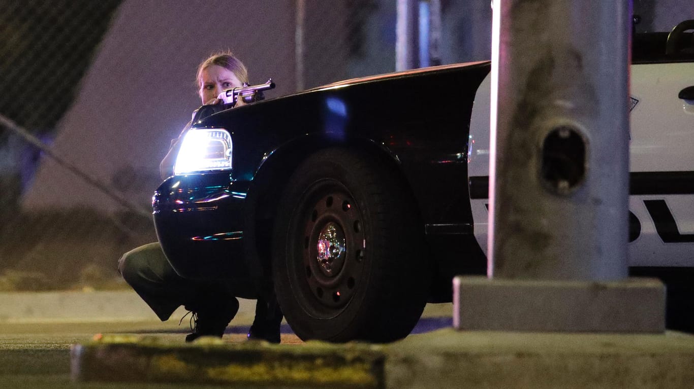 Eine Polizistin geht während der Schießerei hinter einem Fahrzeug in Deckung.