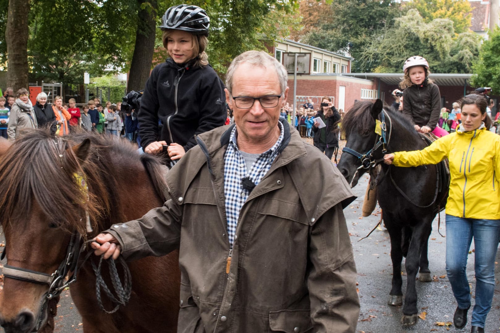 Wanderreiter Hans Watzl und seine beiden Enkelkinder Hannes (l) und Esther auf dem Rücken seiner Pferde. Im Hintegrund sind die Schulkinder zu sehen.