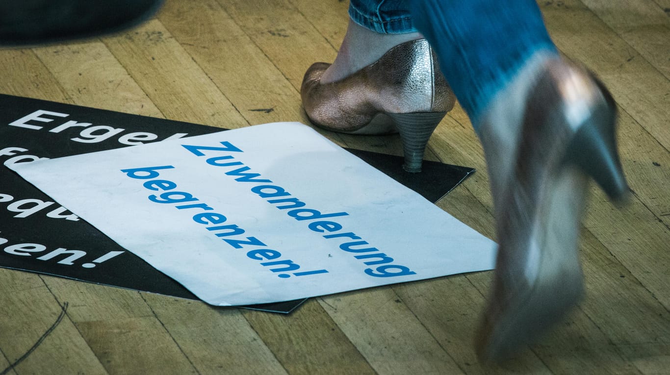 Eine JU-Delegierte läuft an einem auf dem Boden liegendem Schild mit der Forderung "Zuwanderung begrenzen!" vorbei.