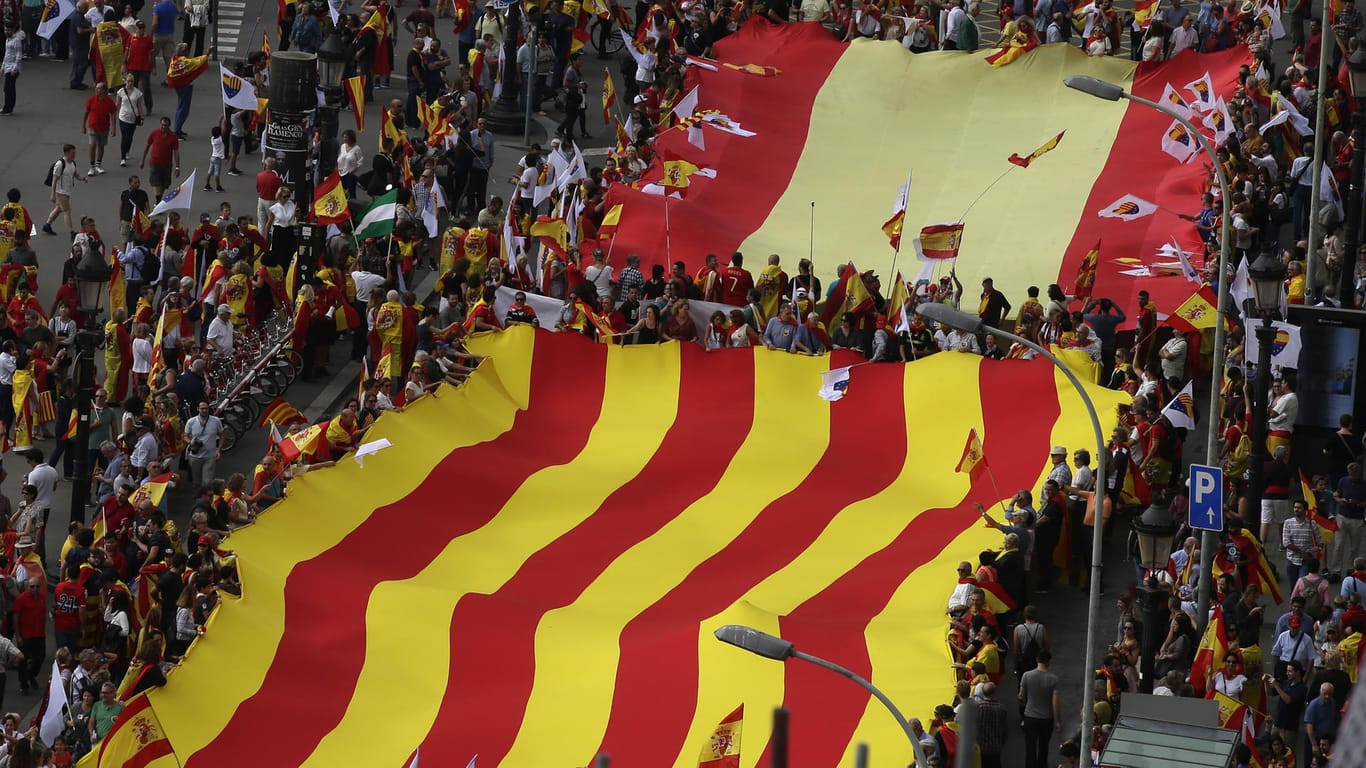 Menschen tragen in Barcelona während des Spanischen Nationalfeiertags eine riesige spanische Flagge und eine Flagge Kataloniens.