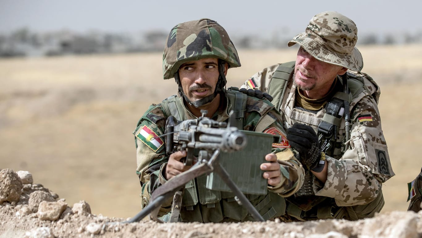 Ein Soldat der Bundeswehr weist einen Peschmerga-Kämpfer an einem Maschinengewehr ein.