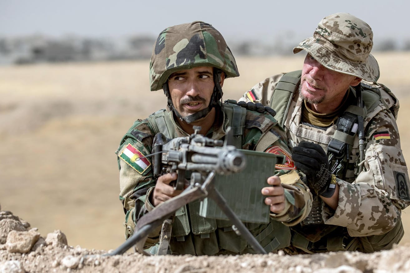 Ein Soldat der Bundeswehr weist einen Peschmerga-Kämpfer an einem Maschinengewehr ein.