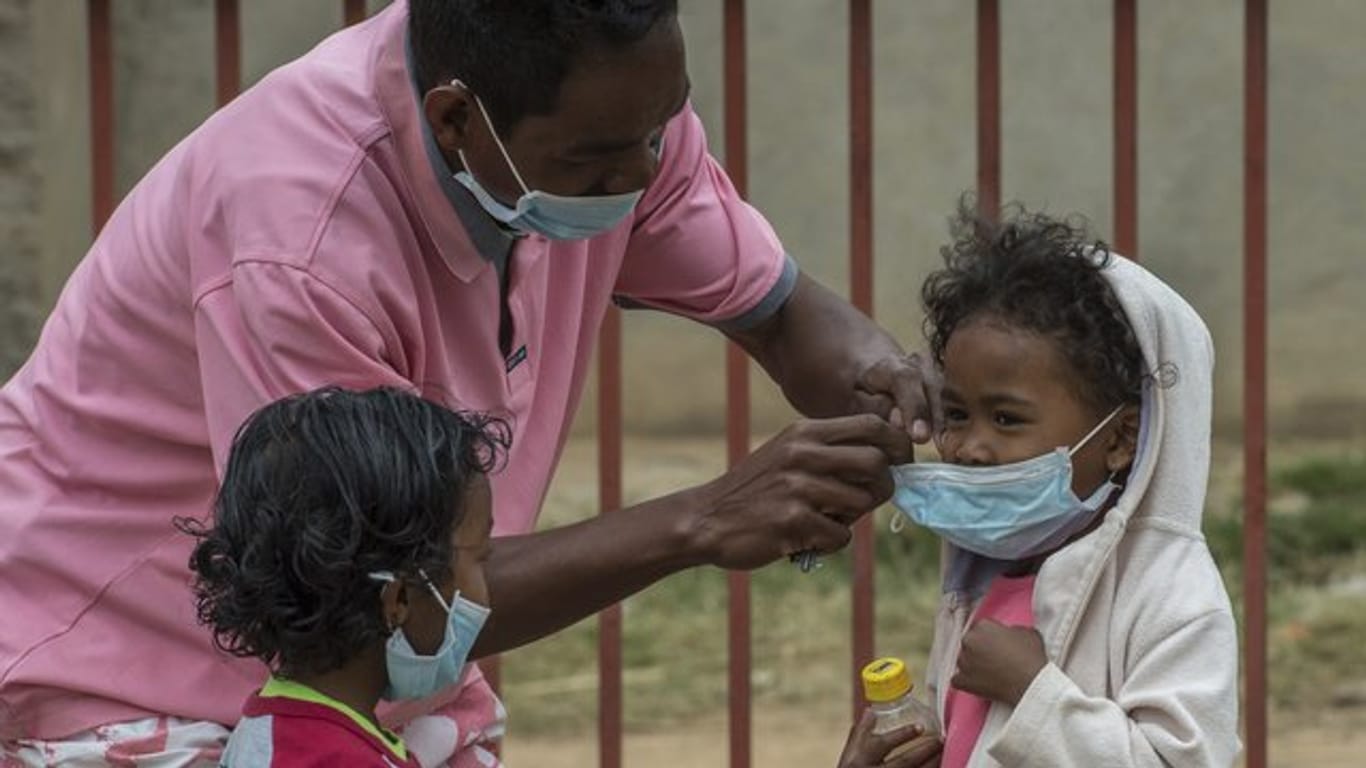 Ein Mann in Antananarivo legt einem Kind einen Mundschutz an.