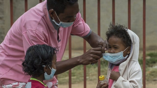 Ein Mann in Antananarivo legt einem Kind einen Mundschutz an.