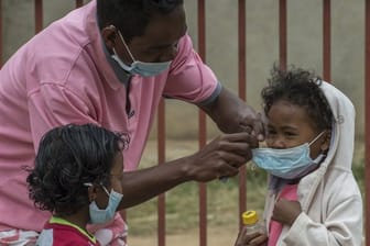 Ein Mann in Antananarivo legt einem Kind einen Mundschutz an.