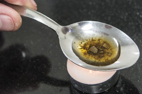 Ein Mann "kocht" sich auf einem Löffel die Dosis für einen Schuss Heroin.