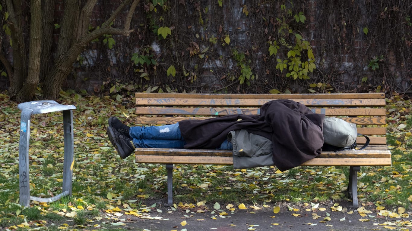 Ein Obdachloser schläft in Berlin auf einer Parkbank.