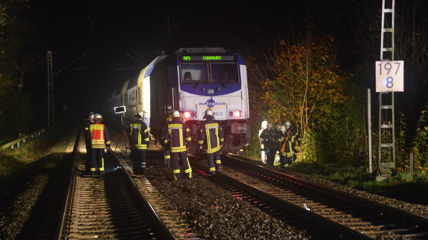 Feuerwehrleute und Polizisten stehen auf den Gleisen im Kreis Stade neben einem Metronom-Zug. Ein Autofahrer ist auf einem Bahnübergang gerammt worden.