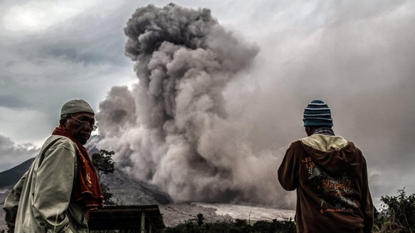 Männer beobachten in Sumatra den Asche speienden Vulkan Sinabung.