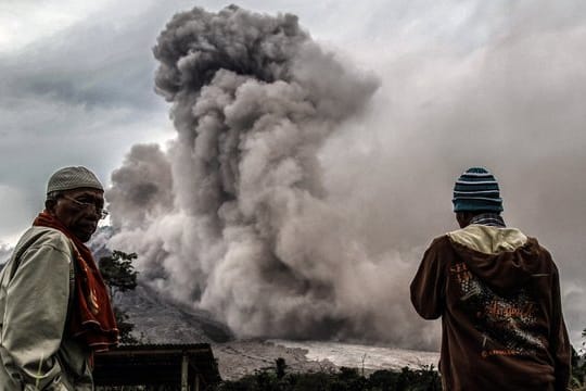 Männer beobachten in Sumatra den Asche speienden Vulkan Sinabung.