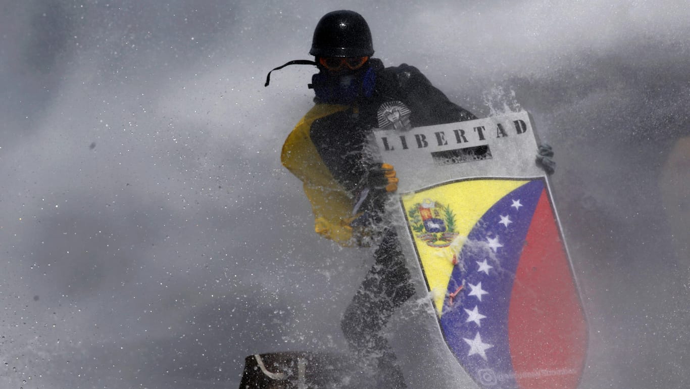 Ein Demonstrant in Venezuela sucht Schutz hinter einem selbstgemachten Schild.