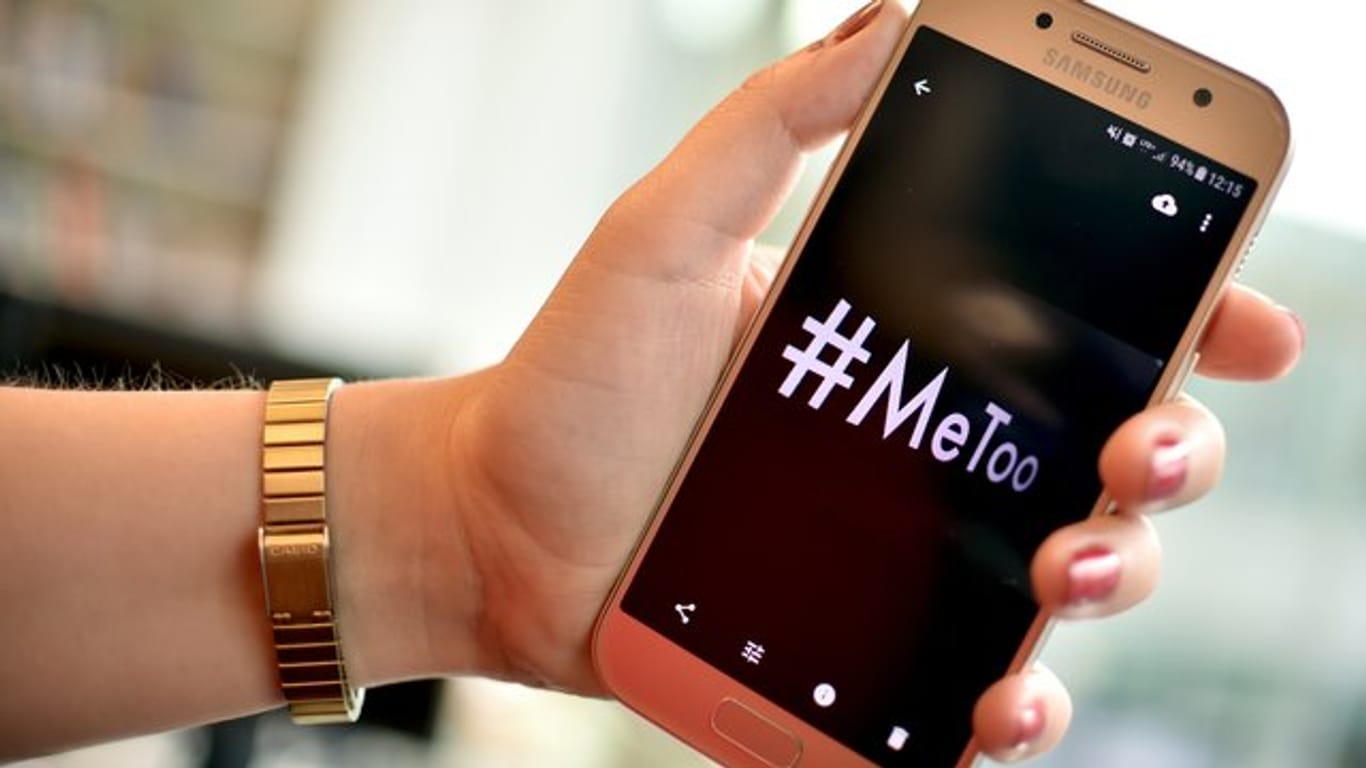 Eine junge Frau hält ein Smartphone mit dem Hashtag "#MeToo".