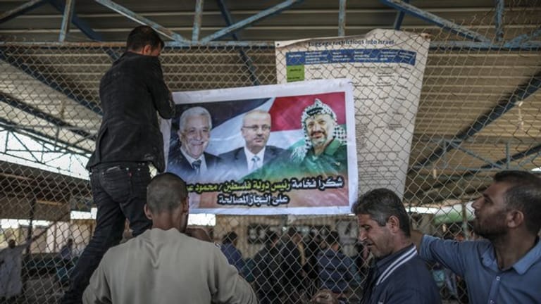 Männer bringen am israelisch-palästinischen Grenzübergang Erez ein Poster mit den Porträts von Palästinenserpräsident Mahmud Abbas (l), Premierminister Rami Hamdallah (M) und dem verstorbenen Palästinenserführer Yasser Arafat an.