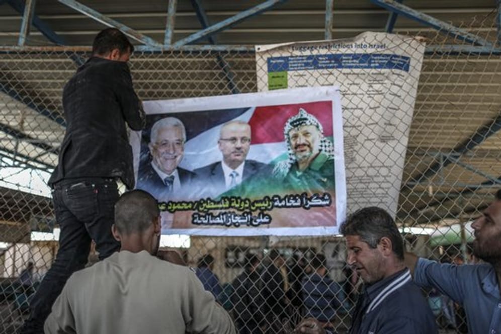 Männer bringen am israelisch-palästinischen Grenzübergang Erez ein Poster mit den Porträts von Palästinenserpräsident Mahmud Abbas (l), Premierminister Rami Hamdallah (M) und dem verstorbenen Palästinenserführer Yasser Arafat an.
