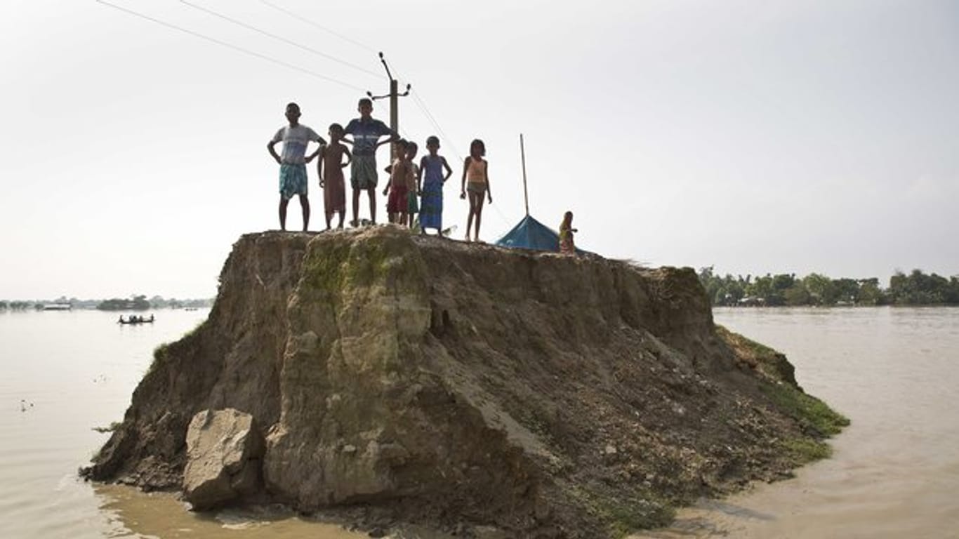 Dorfbewohner warten auf einer von den Überschwemmungen zerstörten Straße in Guwahati in Indien auf Hilfsgüter.