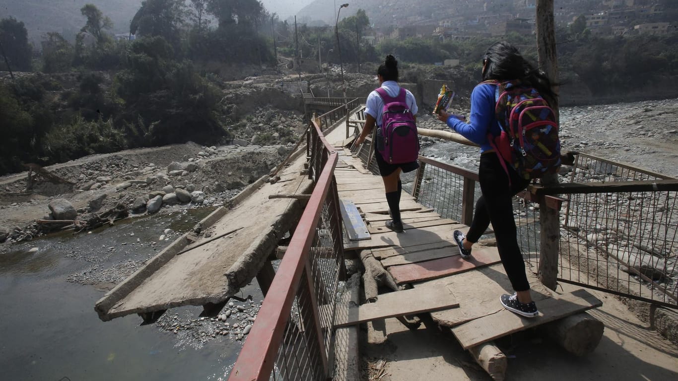 Menschen gehen über eine durch ein Hochwasser zerstörte Brücke in Peru (Archivbild).